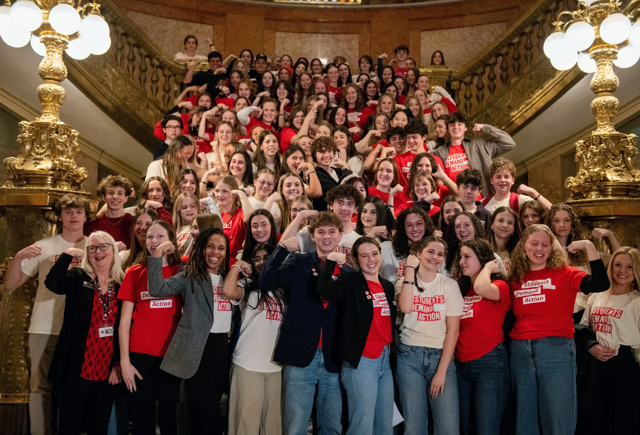 Over 100 students Demand Action volunteers pose for a photo inside the Colorado State Capitol. Many are wearing cream or red Students Demand Action t-shirts and are flexing their biceps to show the power of the movement.