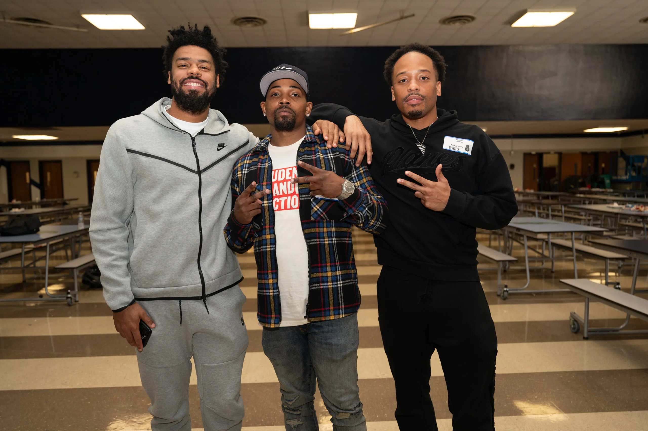 From left to right: Quinn Cook, Neal McDonald, and Justin Murray pose for a photo in the cafeteria of a DMV school during a stop on the Motivating Our Future Summit Tour.