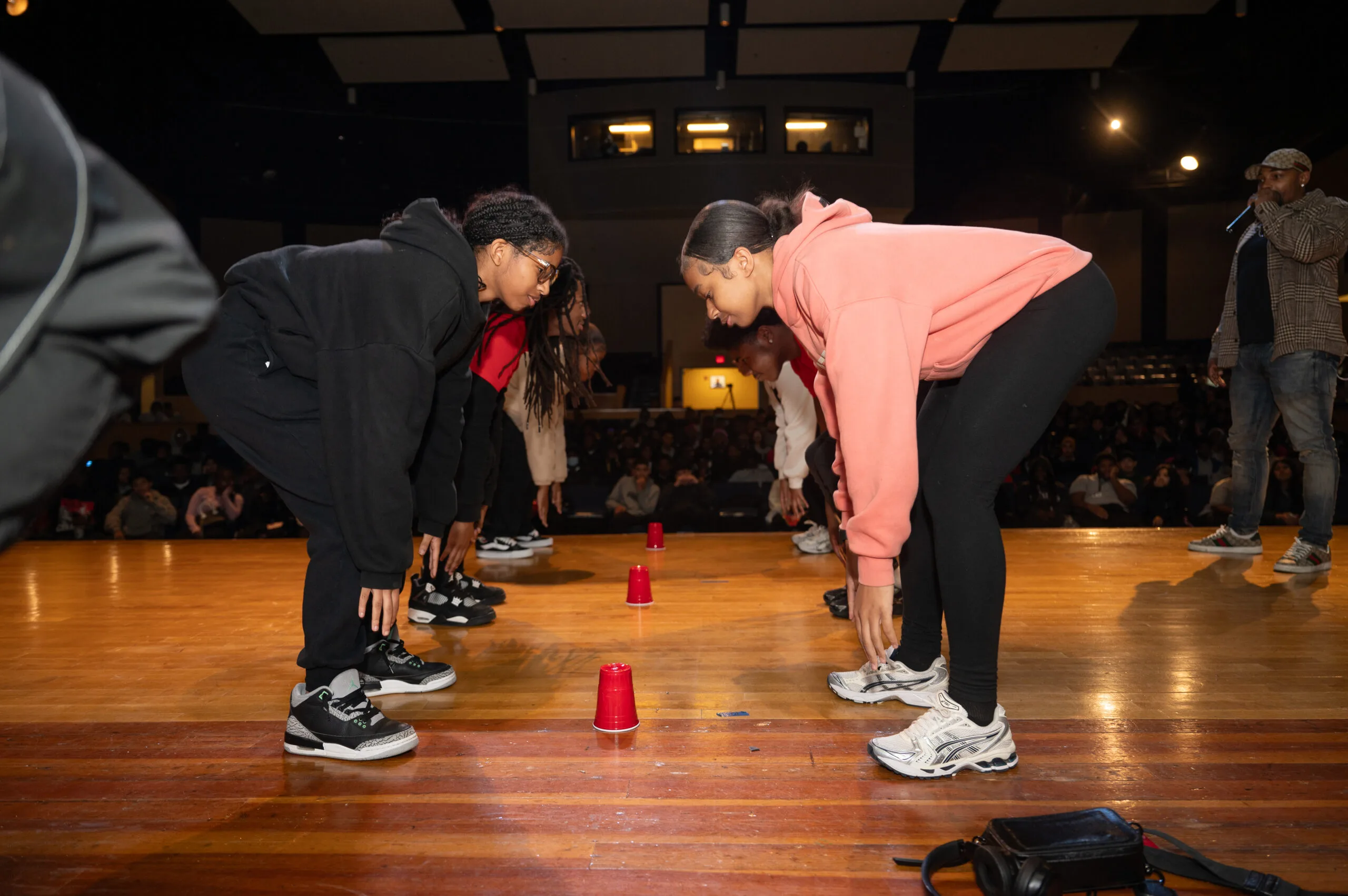 Six students stand in two rows of three, standing across from each other in pairs, as they prepare to try to grab a red plastic cup during an audience participation game at a Motivating Our Future tour stop.
