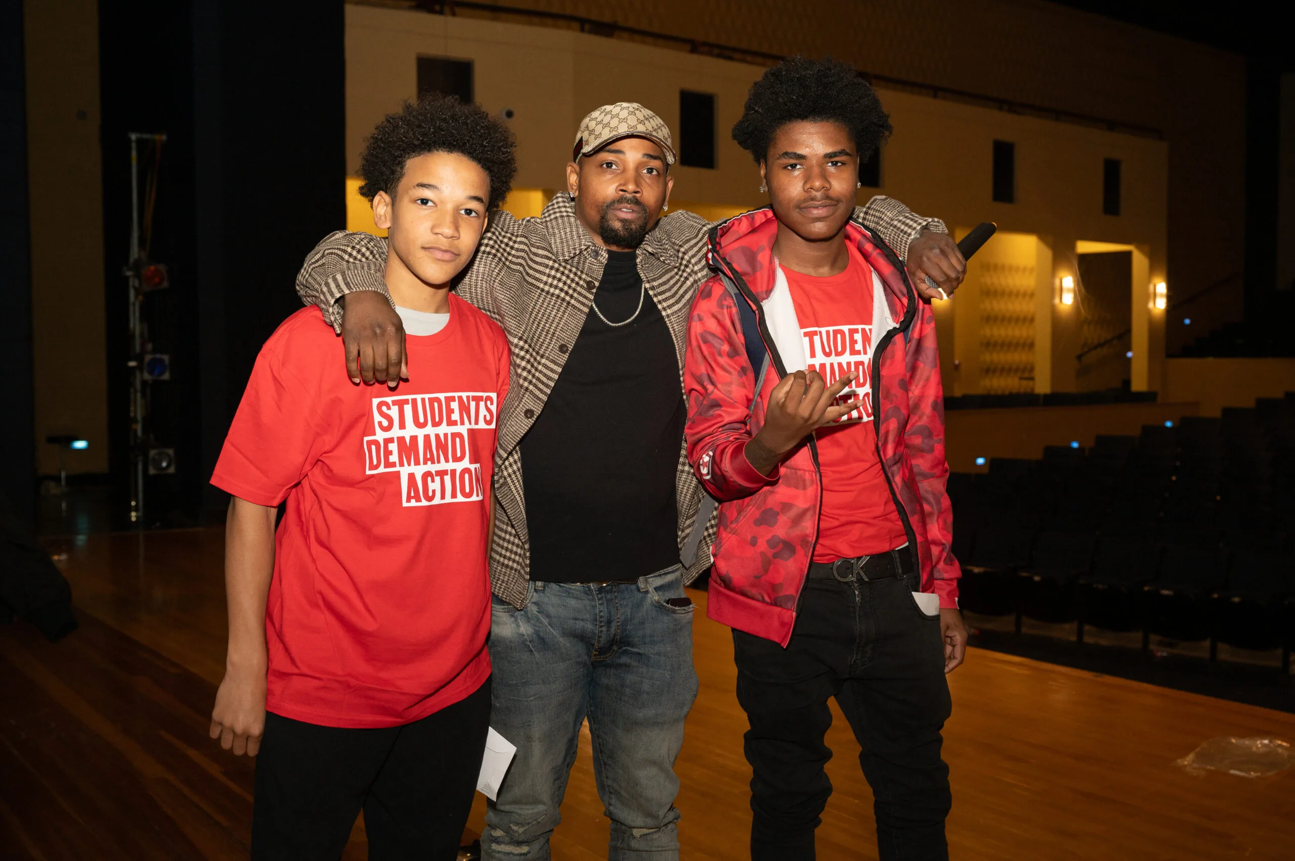 Neal McDonald (center) poses for a photo on stage with two students wearing red Students Demand Action t-shirts.