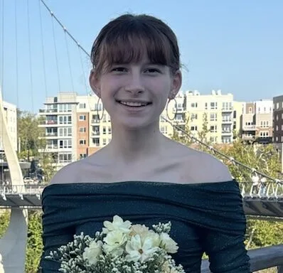Leah VanBuskirk, a Students Demand Action Text Team Captain, poses for a photo while wearing a formal long-sleeved green dress and carrying a bouquet of flowers.