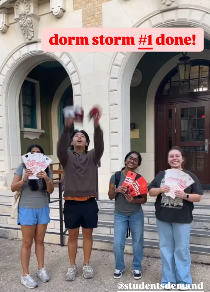 Four Students Demand Action volunteers at the University of Austin Texas celebrate being done with their first "dorm storm." They hold door-knob placards with literature about Students Demand Action printed on them. The top of the photo is captioned "dorm storm #1 done!" At the bottom right, @studentsdemand is tagged in white text.