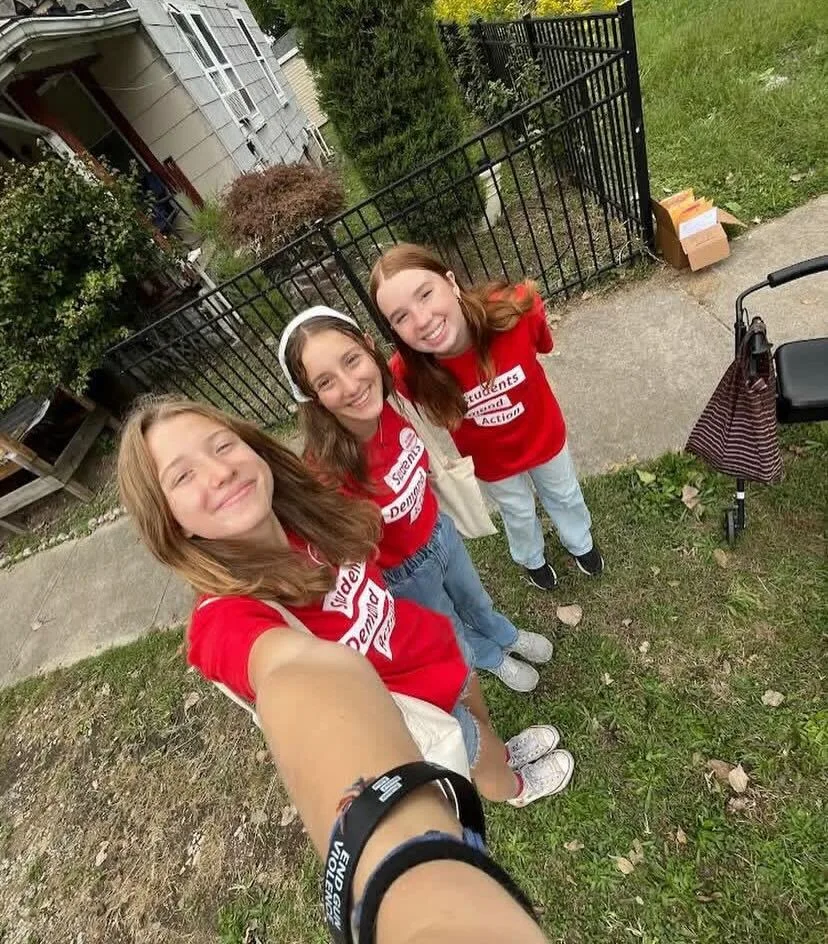 A group of three students take a selfie in .5 mode. They are wearing red Students Demand Action t-shirts. The student taking the photo has her arm extended; a black bracelet that says "end gun violence" is visible on her wrist.