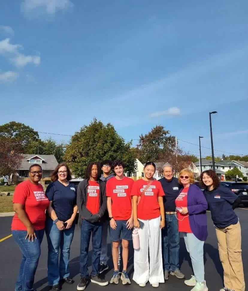A group of nine total Moms Demand Action and Students Demand Action volunteers, who are canvassing, pose for a photo in a parking lot.