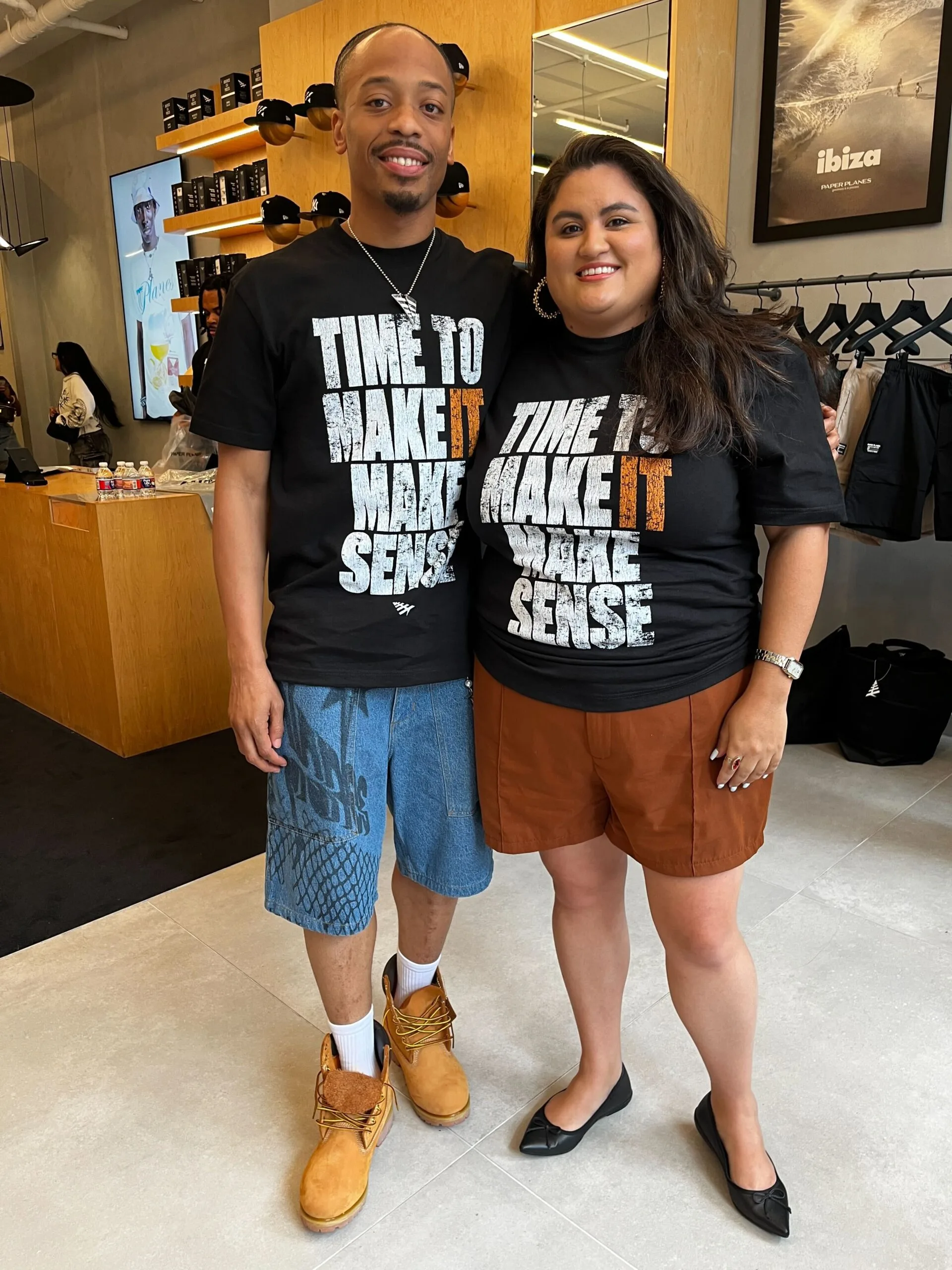Justin Murray and Andrea Azalia pose for a photo at the Paper Planes pop-up event in honor of Neal McDonald. Both are wearing the black "Time to Make It Make Sense" t-shirt.