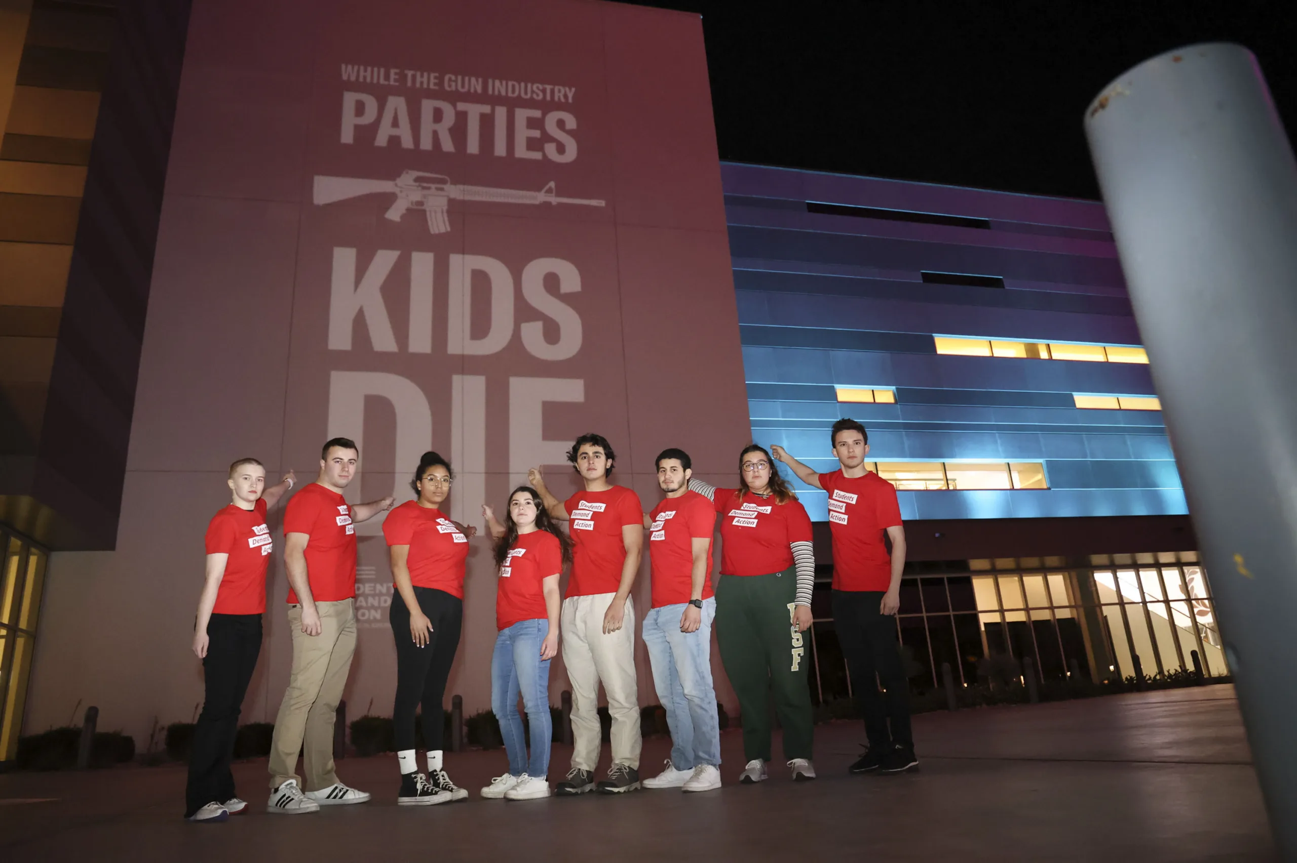 Students Demand Action volunteers wearing red t-shirts and standing in front of the SHOT Show wall installation: "While the gun industry parties, kids die"
