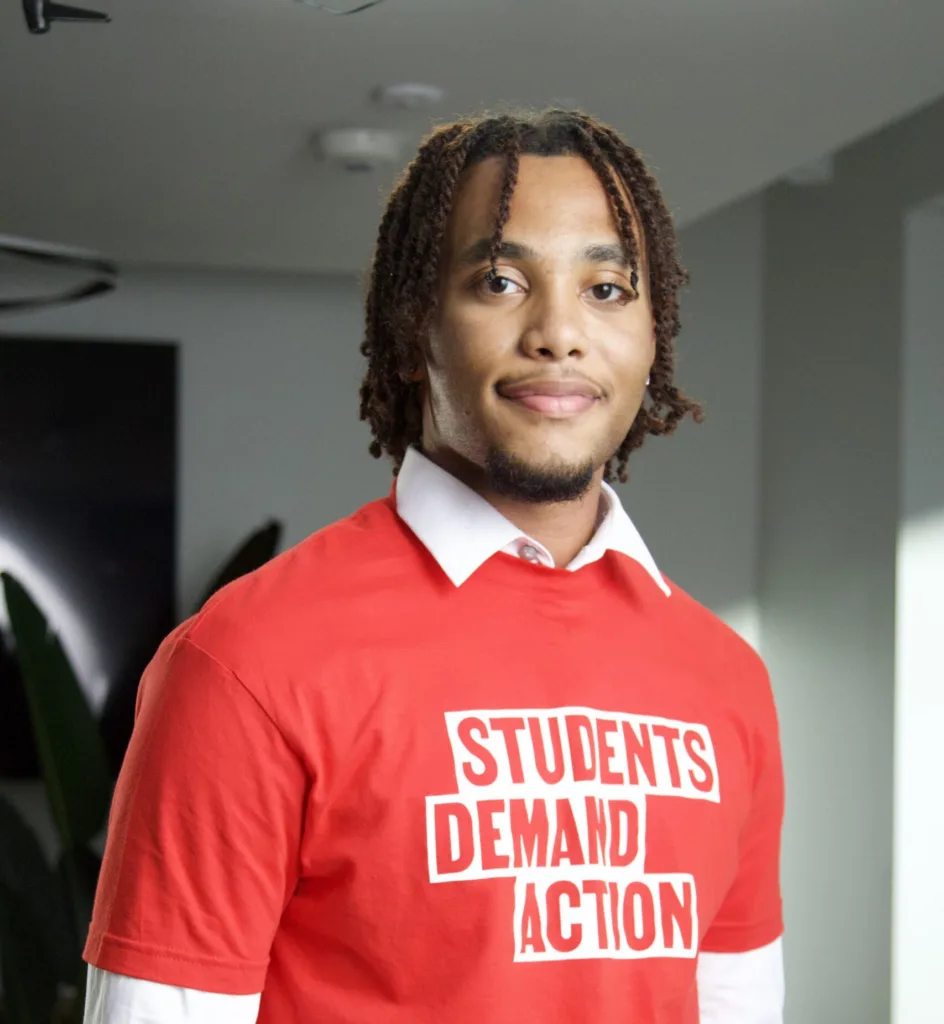Ivan Walker, one of the Students Demand Action Creators, poses for a professional photo. He is wearing a collared, long-sleeve white shirt with a red Students Demand Action t-shirt layered over top.