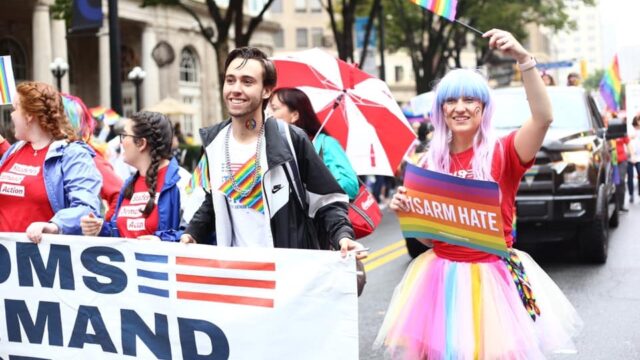 Students Demand Action volunteer John Peterson holds a Moms Demand Action banner at a Pride march