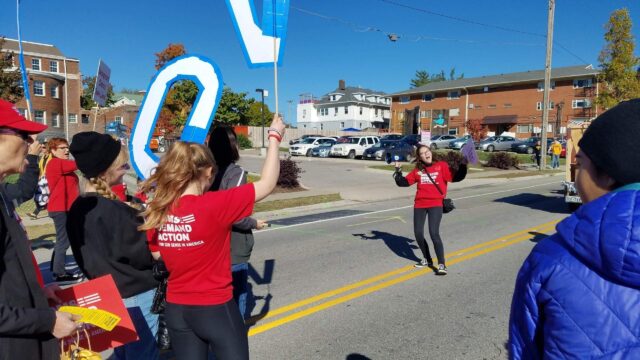 Students Demand Action volunteer Celena Schmolzi smiling while holding a megaphone at an outdoor event. She is leading a march of other Students Demand Action volunteers