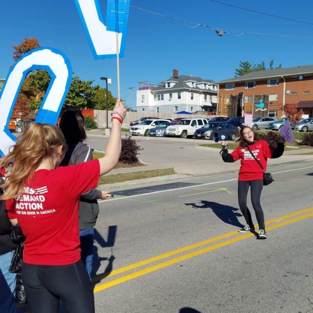 Students Demand Action volunteer Celena Schmolzi smiling while holding a megaphone at an outdoor event. She is leading a march of other Students Demand Action volunteers