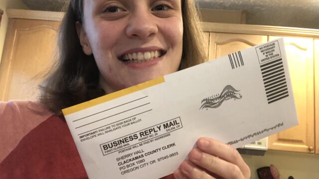 A Students Demand Action volunteer smiles while taking a selfie with their mail-in ballot