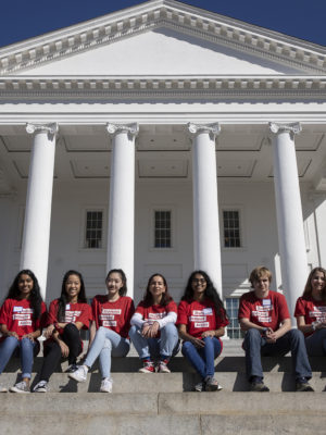 A group of nine Students Demand Action volunteers sit in front of the Capitol at Richmond Advocacy Day