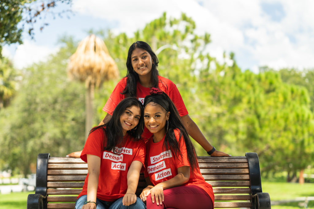 Tampa Summer Leadership Academy leaders Neha Bangalore, Azra Khan, and Ashanti Johnson pose for photos around a park bench