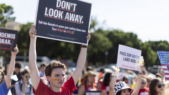 A person in a Students Demand Action shirt holds up a Don't Look Away sign in a crowd at a rally in Washington, DC in June 2022