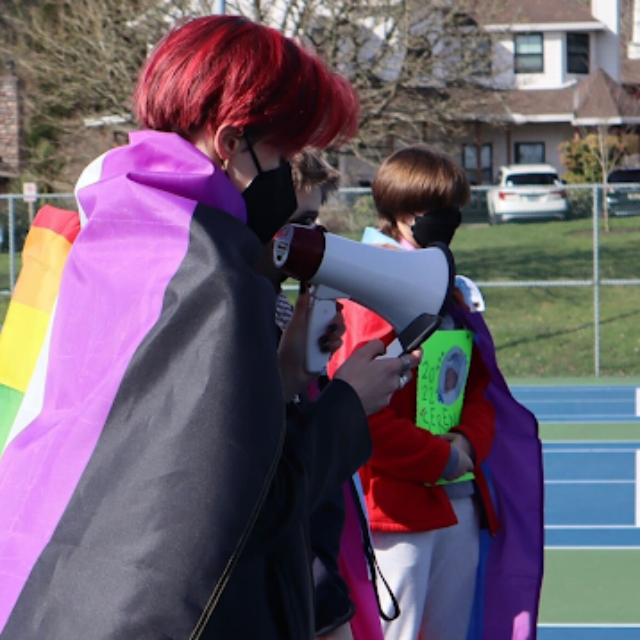 Flynn Williams wearing a Pride flag cape and holding a megaphone
