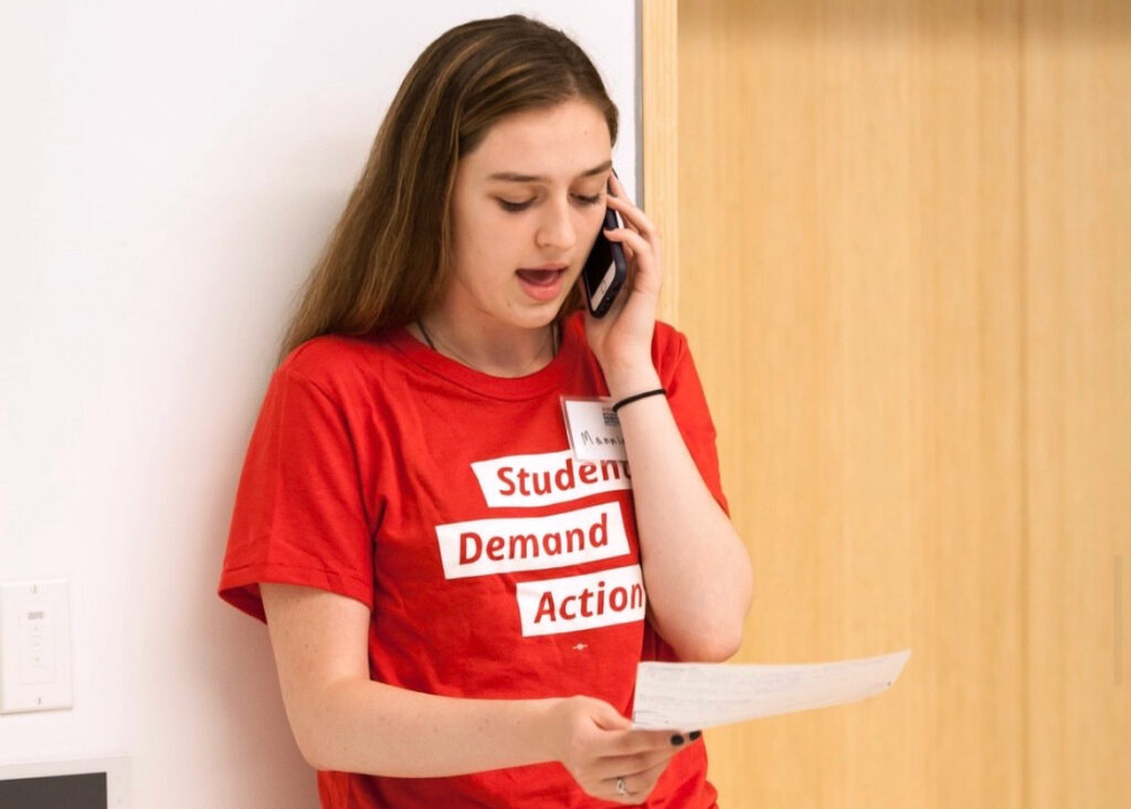 A Students Demand Action volunteer speaks into a cell phone while holding a script