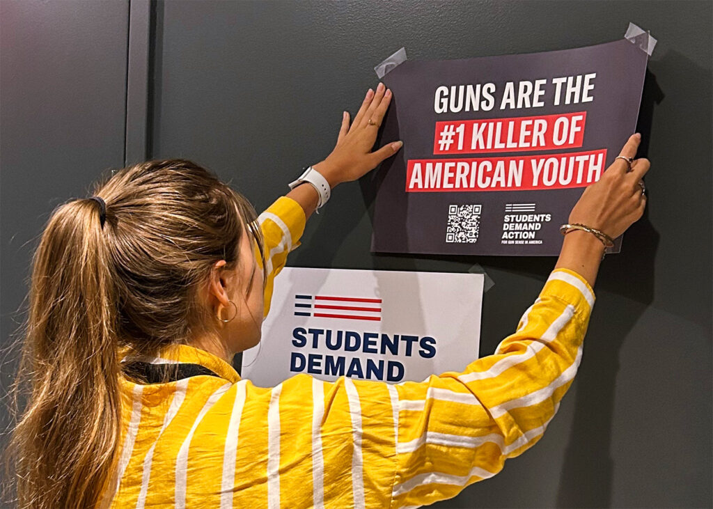 A Students Demand Action volunteer hangs a placard on the wall that reads "Guns are the #1 killer of American youth."