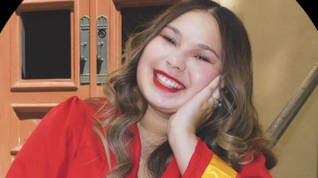 Leighanne Muñoz, a student volunteer, poses for a photo. She rests her head on her left hand and is wearing a red graduation robe with a gold ribbon that circles the sleeve about an inch from the cuff. Her long hair is curled and parted in the middle.