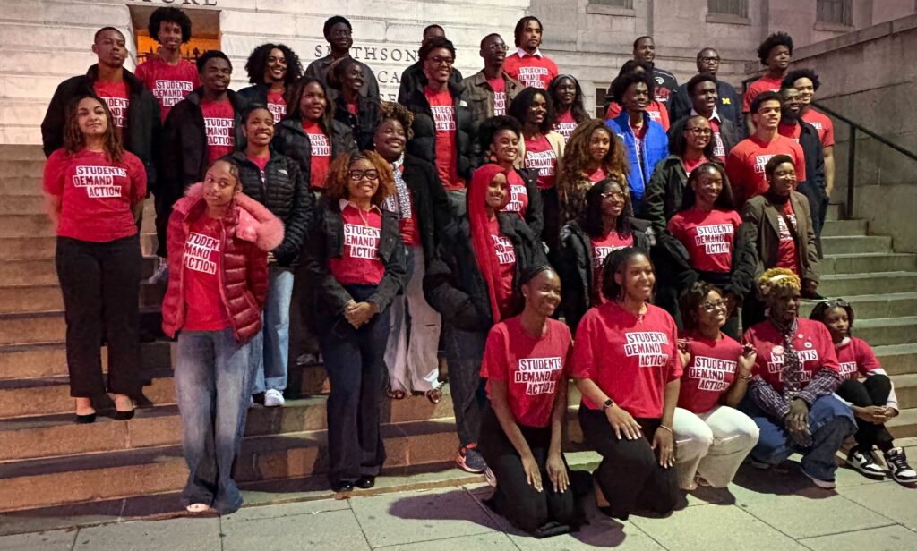 Approximately 40 Young Changemaker Summit college student attendees pose for a photo on the steps of the National Portrait Gallery in the evening. They are all wearing red Students Demand Action t-shirts; most wear jackets.