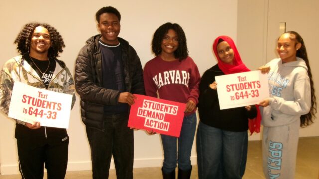 Five students pose for a photo during the Young Changemakers Summit. They hold Students Demand Action signs that say 